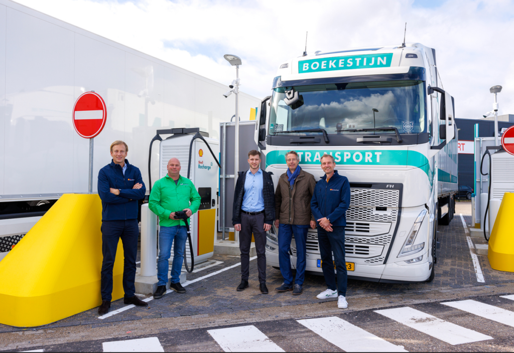 Foto van vijf medewerkers van Boekestijn transport voor een Boekestijn vrachtwagen naast een elektrisch oplaadpunt van Shell