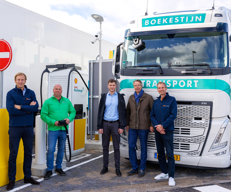 Foto van vijf medewerkers van Boekestijn transport voor een Boekestijn vrachtwagen naast een elektrisch oplaadpunt van Shell